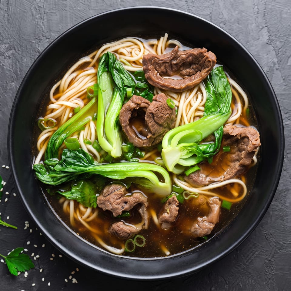 Close-up of a black bowl filled with beef noodle soup, bok choy, and green onions.